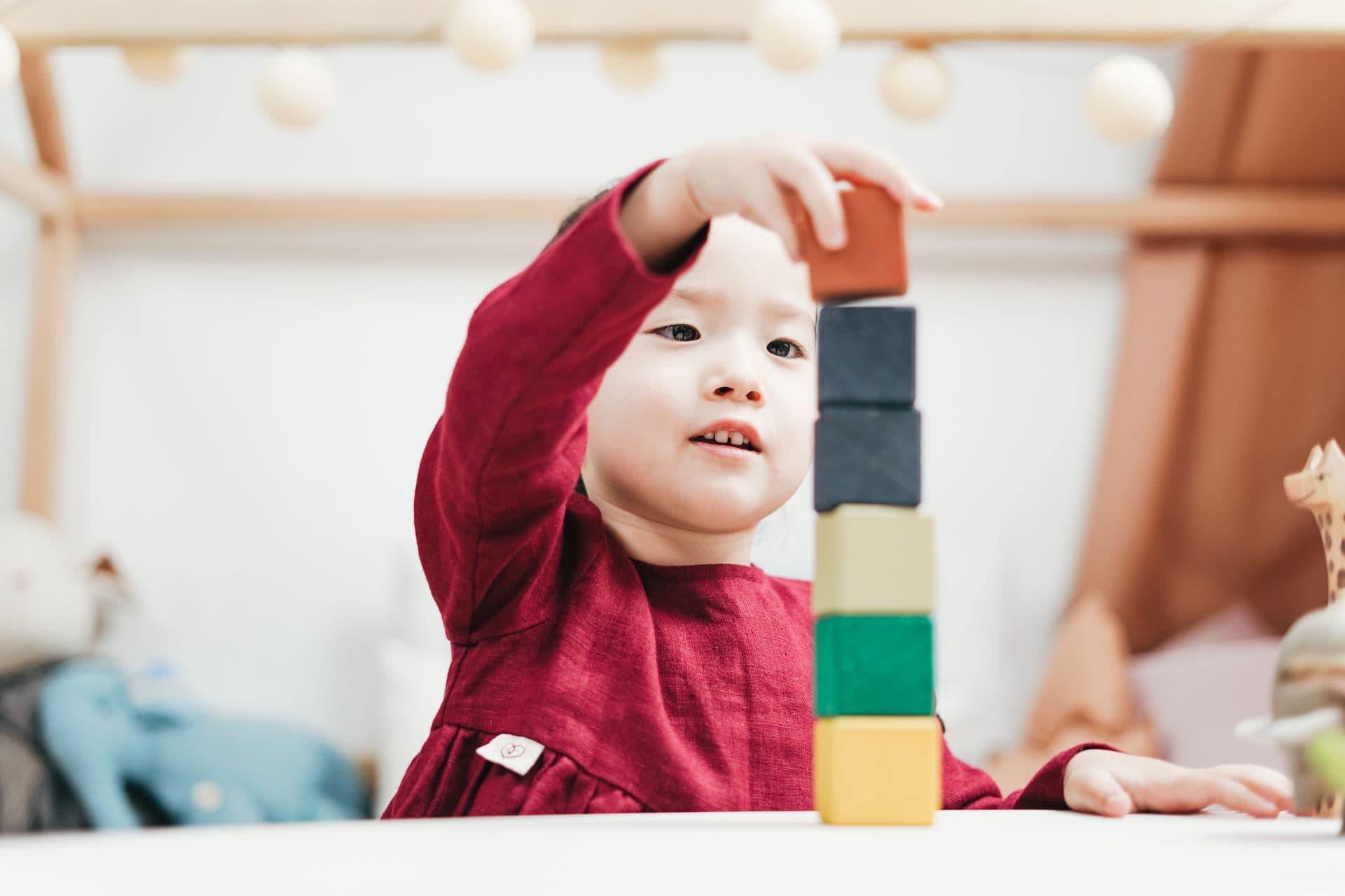 A young child reaching out to place a wooden block on top of a stack of coloured blocks at a table.
