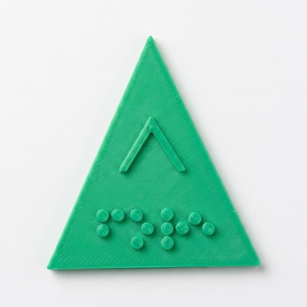 The green triangular cap up close, with a raised upward chevron and the Braille for “up” below it.