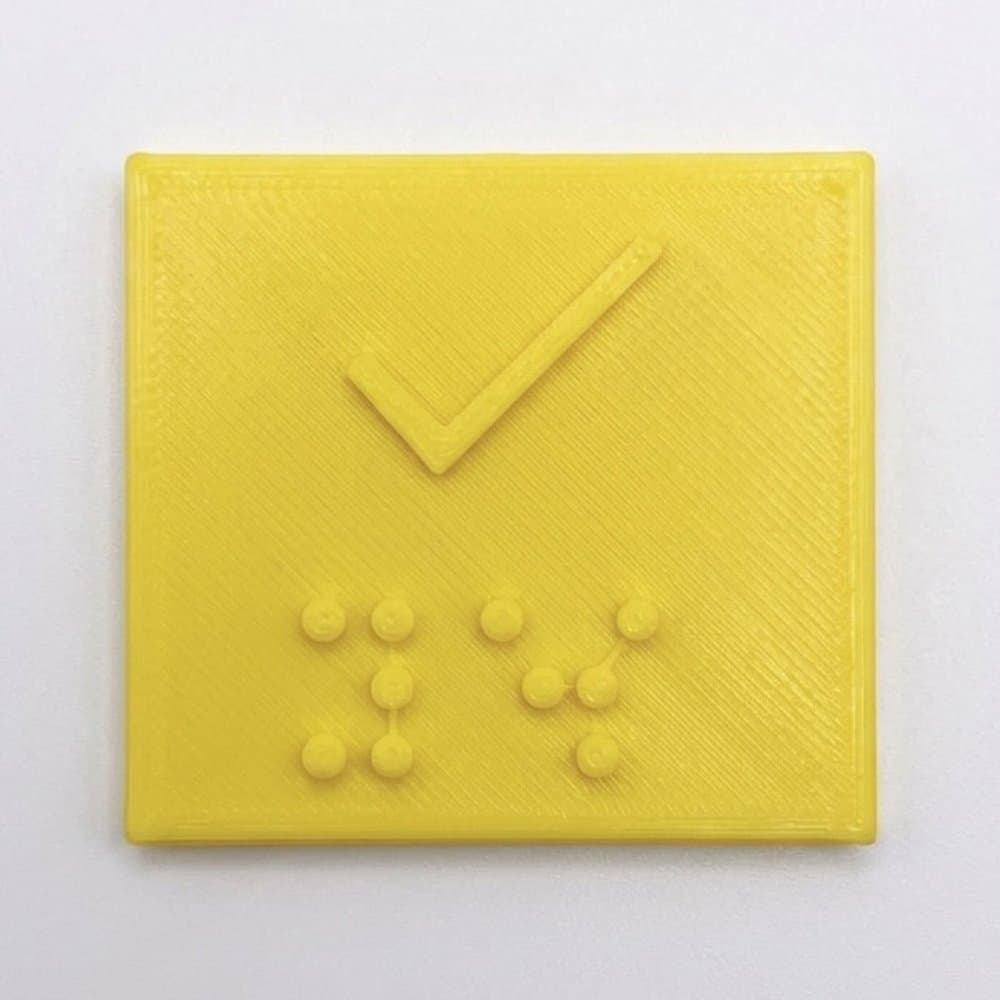 The yellow square cap up close, with a raised tick and the Braille for “yes” below it.