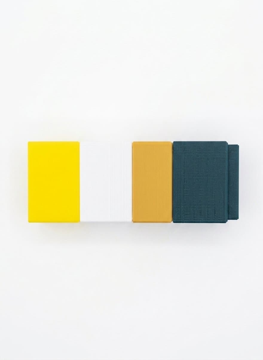 Four cubes snapped together in a row — yellow, white, mustard and dark teal — seen from the side.